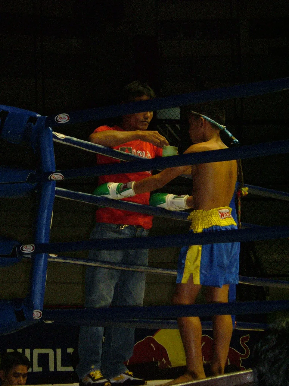 A young Muay Thai fighter with a corner man before a bout, wearing the mongkol headband